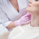 Calm young Caucasian woman getting dermal filler injection into wrinkles on her neck